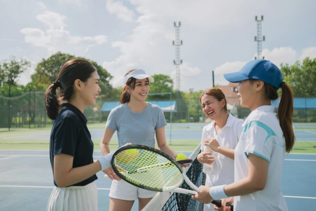 Happy asian young friendship talking and resting after match on the outdoor tennis court on a bright sunny day.